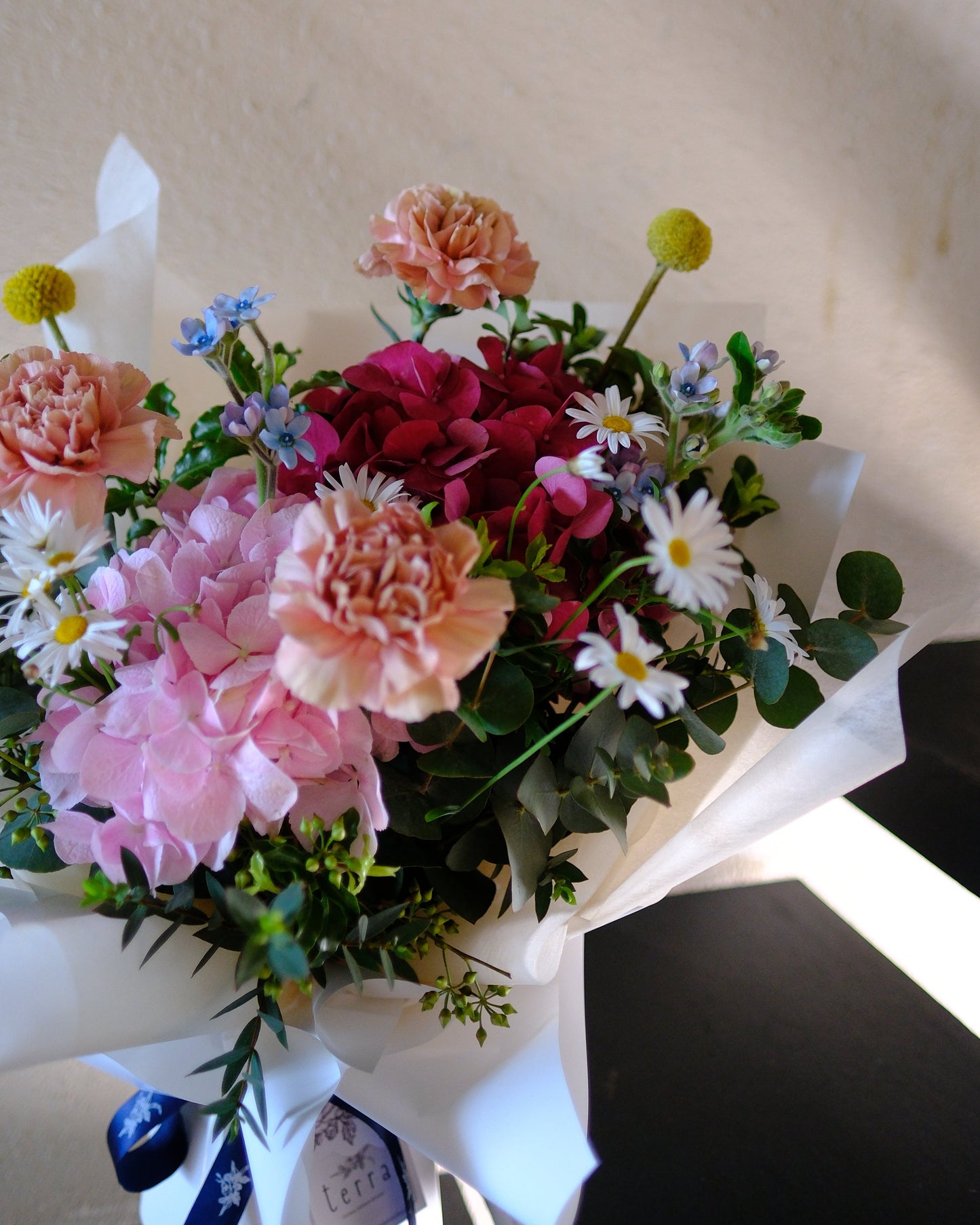 Playful and vibrant Motherâ's Day bouquet with dusty pink Dutch carnations, pink and red hydrangeas, Margarite daisies, and billy buttons designed for the fun-loving mum.