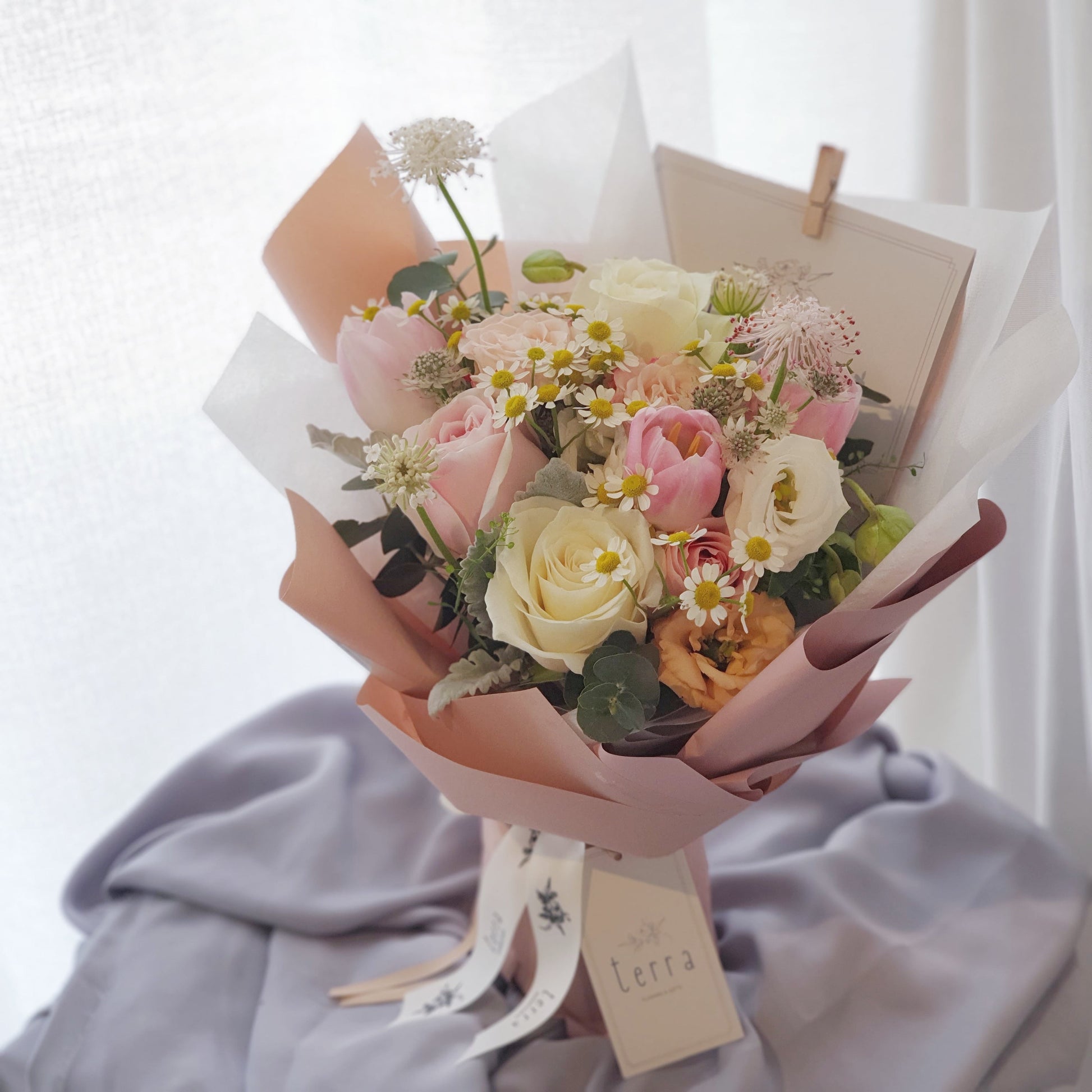 Bouquet of pastel flowers like roses, daisies, tulips wrapped in pink paper 