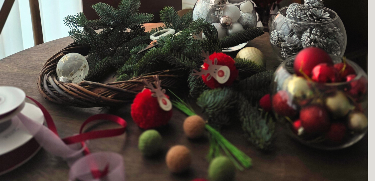 Decorative table setting with Christmas ornaments and greenery on a wooden table.