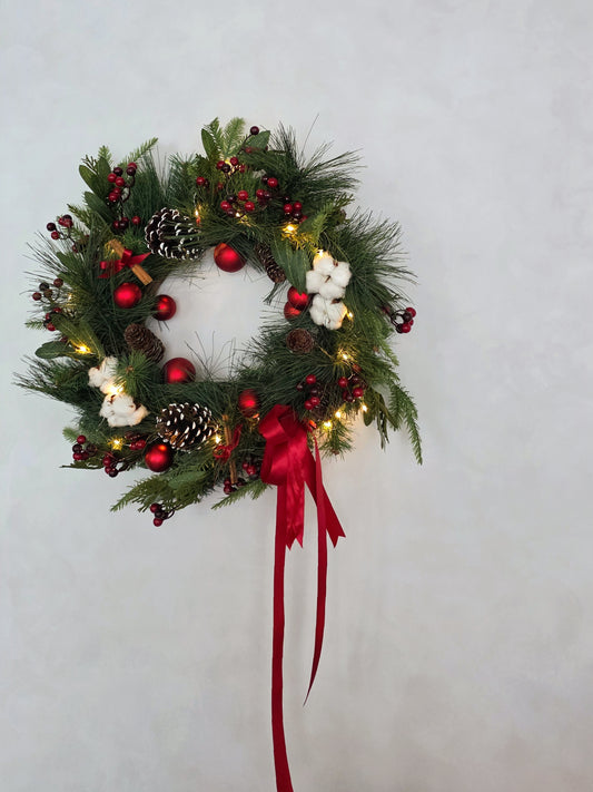 Decorative Christmas wreath with lights, berries, pine cones, cinnamon sticks and a red ribbon