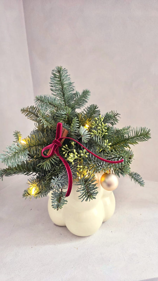 Small Christmas tree with lights, ribbons, and ornaments on a neutral background