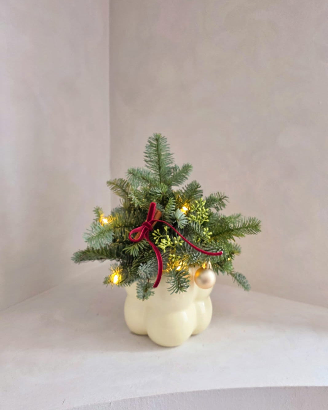 Decorative Christmas tree with lights and a red bow in a white ceramic pot on a light background