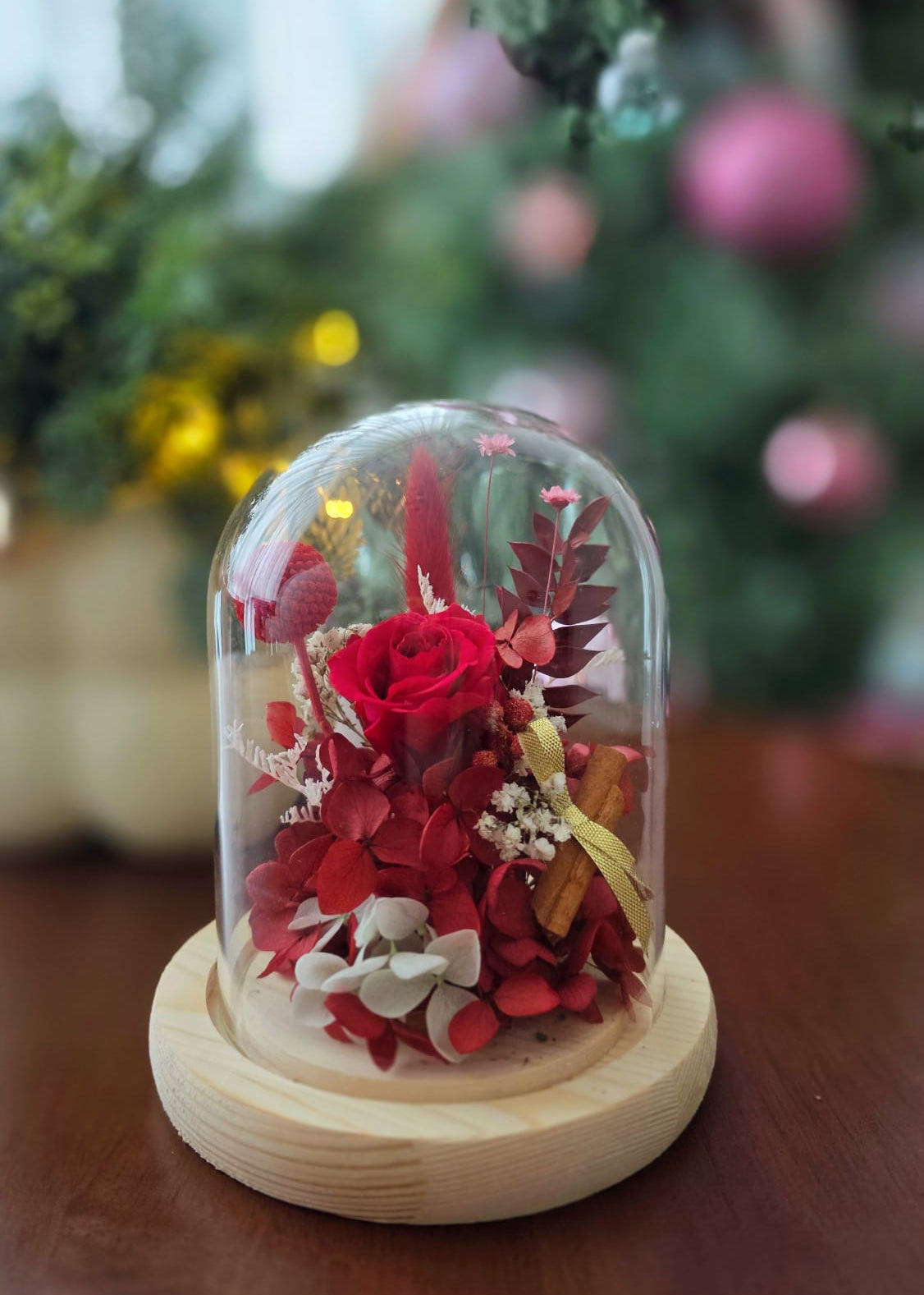 Decorative glass dome with flowers on a wooden base against a blurred floral background