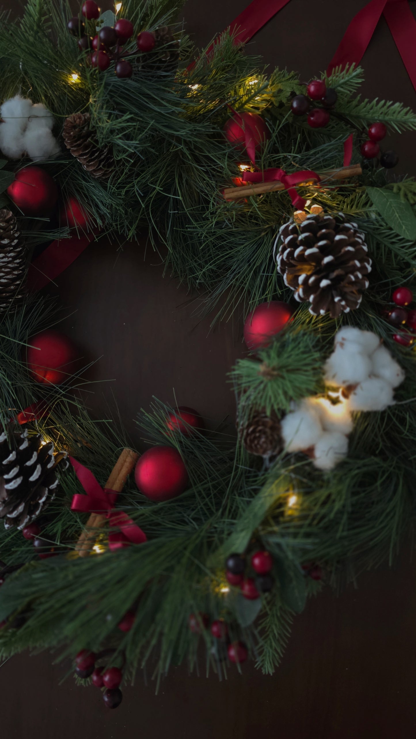 Christmas wreath with pine cones, berries, and lights on a dark background