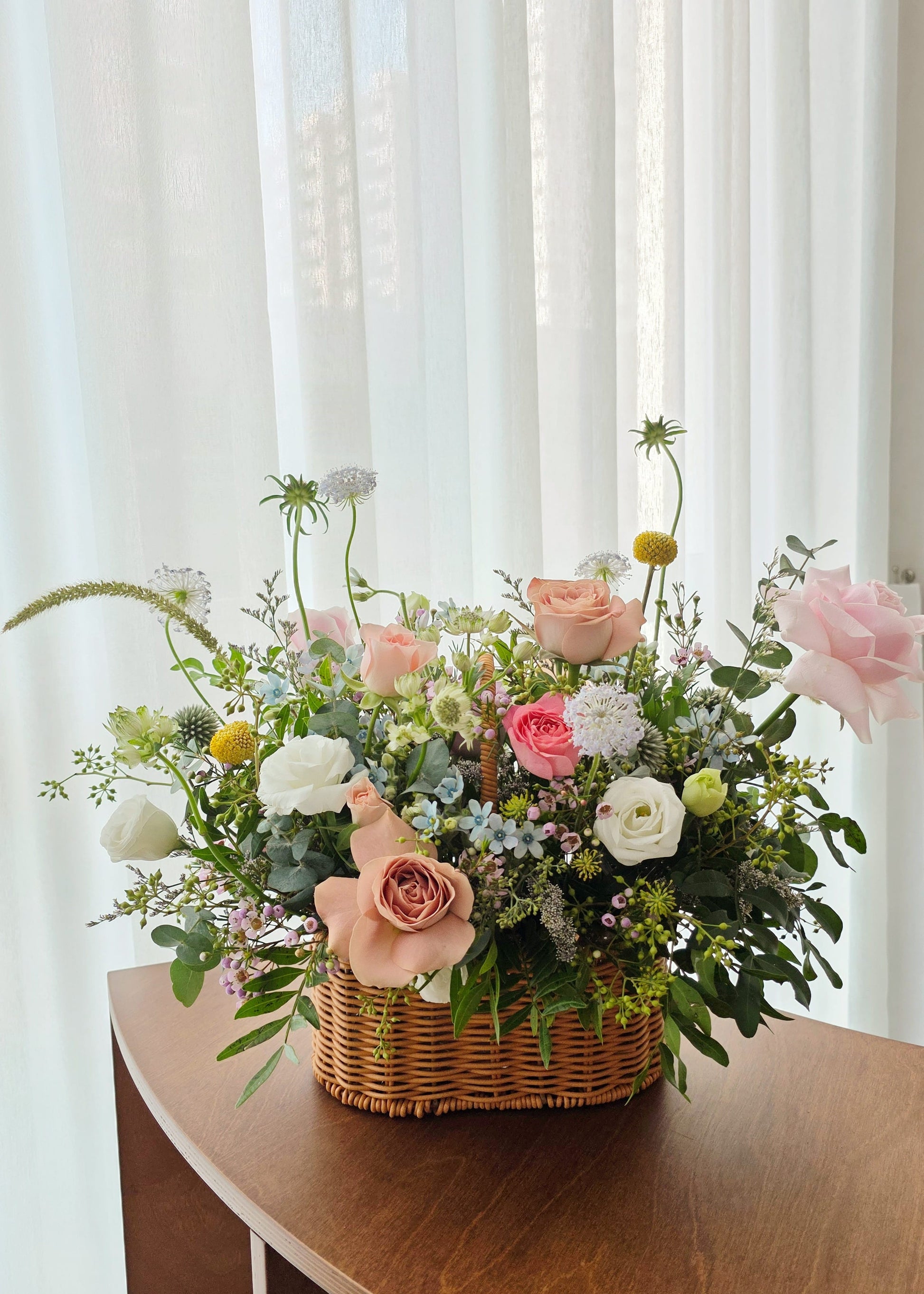 Garden Style Floral arrangement with roses, eustomas and small filler flowers in a woven basket on a wooden table 