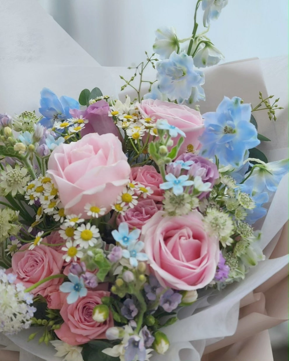 Bouquet of pink, blue, and white flowers like roses, oxypetalum, delphiniums with greenery like eucalyptus on a light background