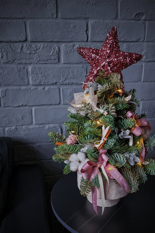 Decorative Christmas tree with a pink star on top against a gray brick wall.