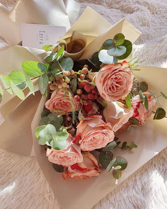 Close-up flatlay of The Enigmatic Muse bouquet — cappuccino and menta roses with Berzelia berries and eucalyptus, wrapped in cream paper with Terra gift card, Singapore