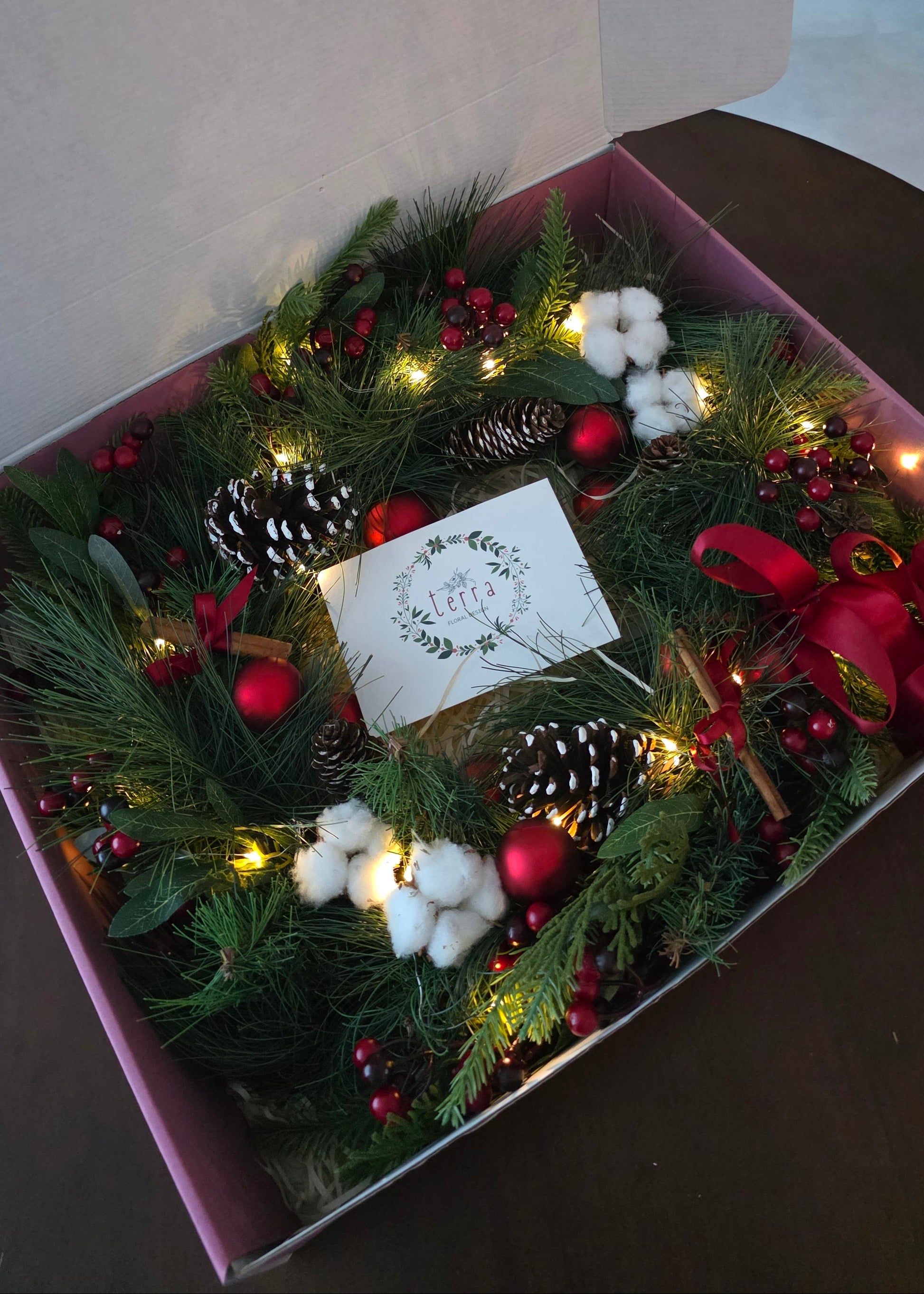 Decorative Christmas wreath with lights and pinecones in a gift box with christmas card.