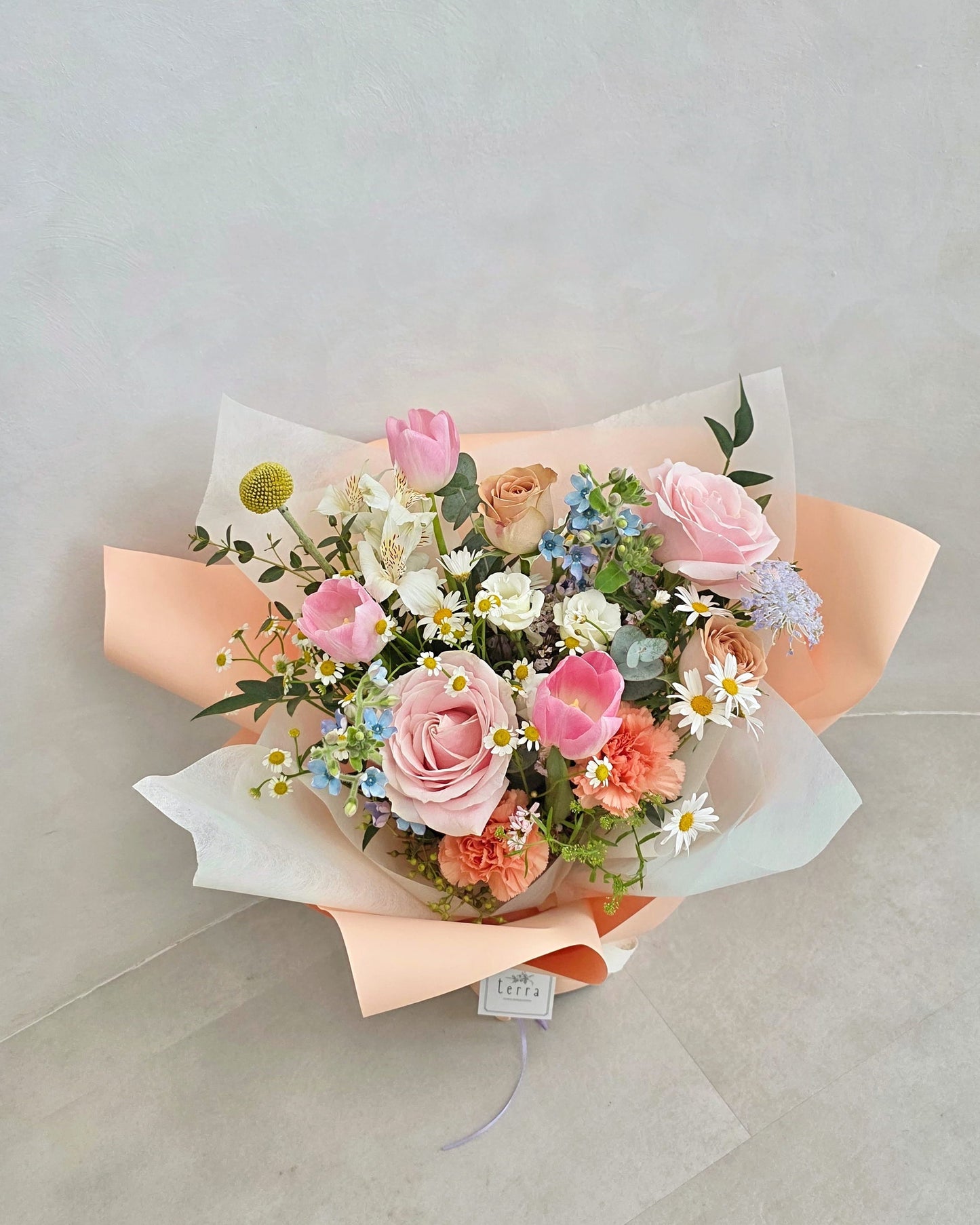 Close-up of Her Garden Mother's Day bouquet featuring soft pink roses, blush tulips and seasonal wildflowers wrapped in layered peach paper — Flowers by Terra