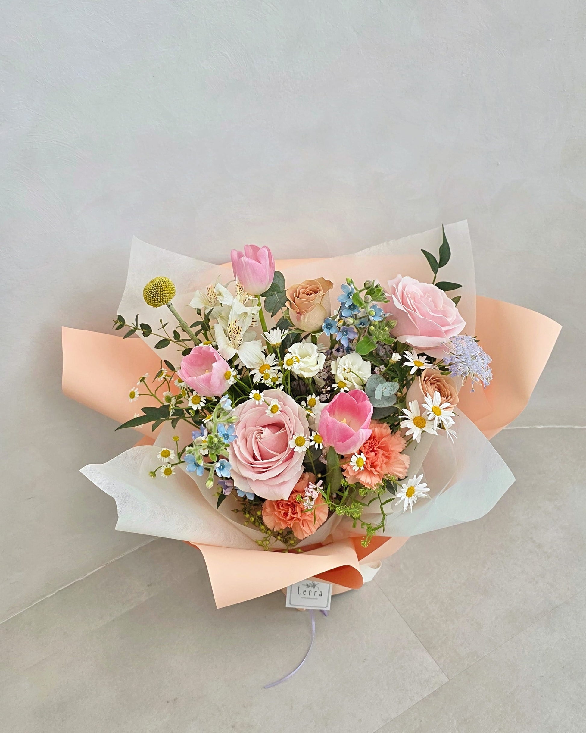 Close-up of Her Garden Mother's Day bouquet featuring soft pink roses, blush tulips and seasonal wildflowers wrapped in layered peach paper — Flowers by Terra