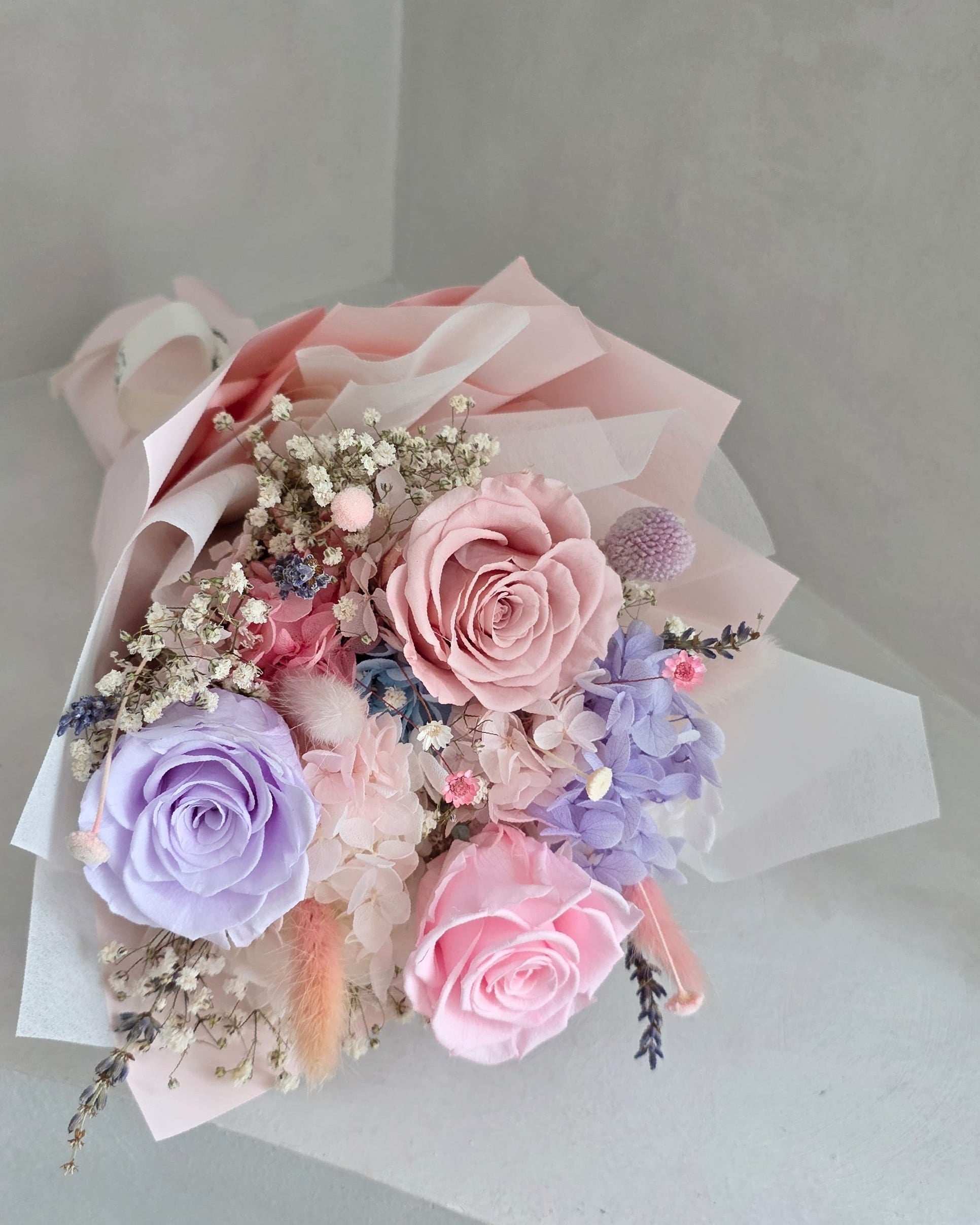 Full view of pastel preserved rose bouquet styled in layered translucent wrapping