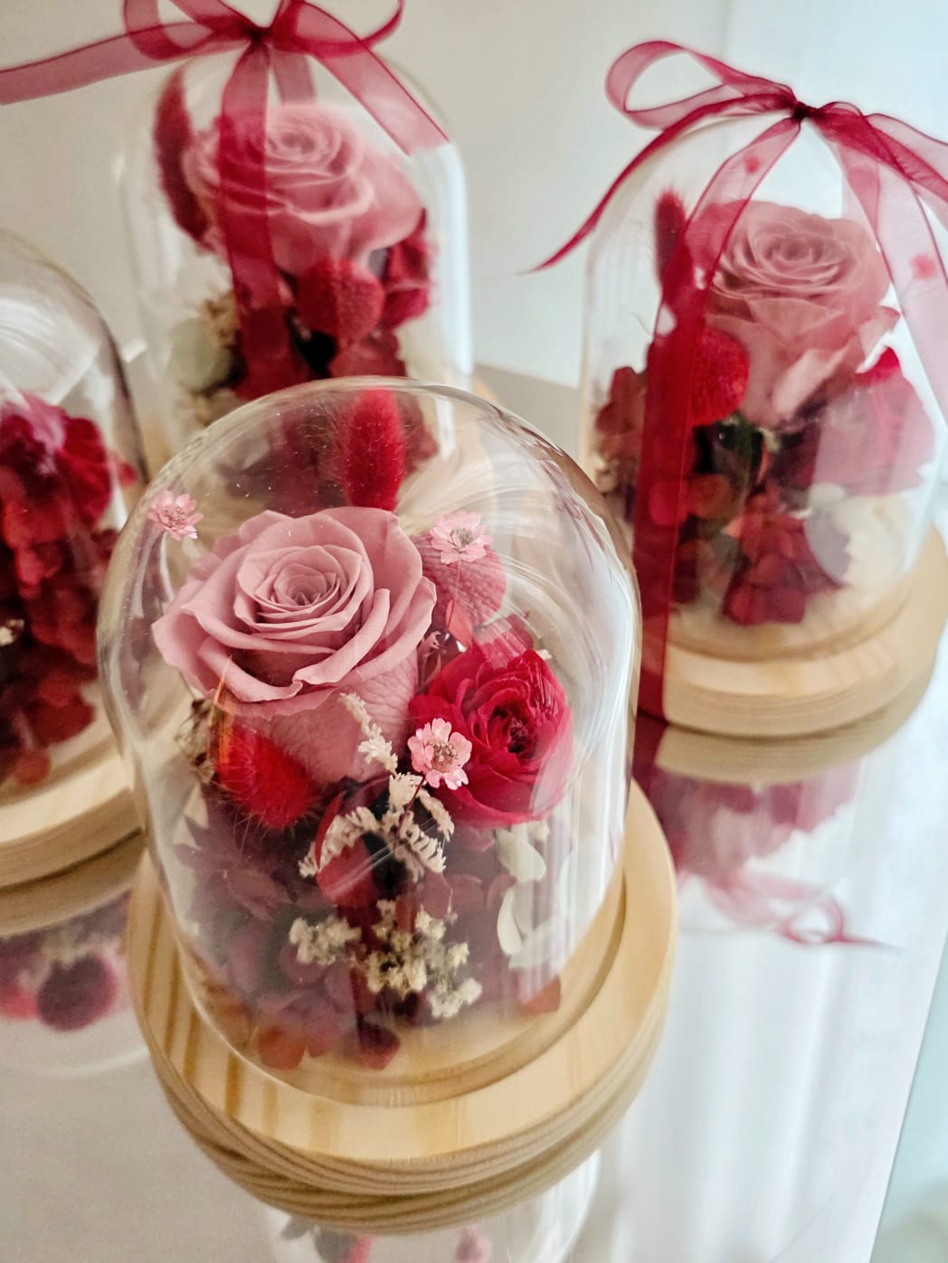 Preserved rose and hydrangea arrangement in a glass dome with wooden base